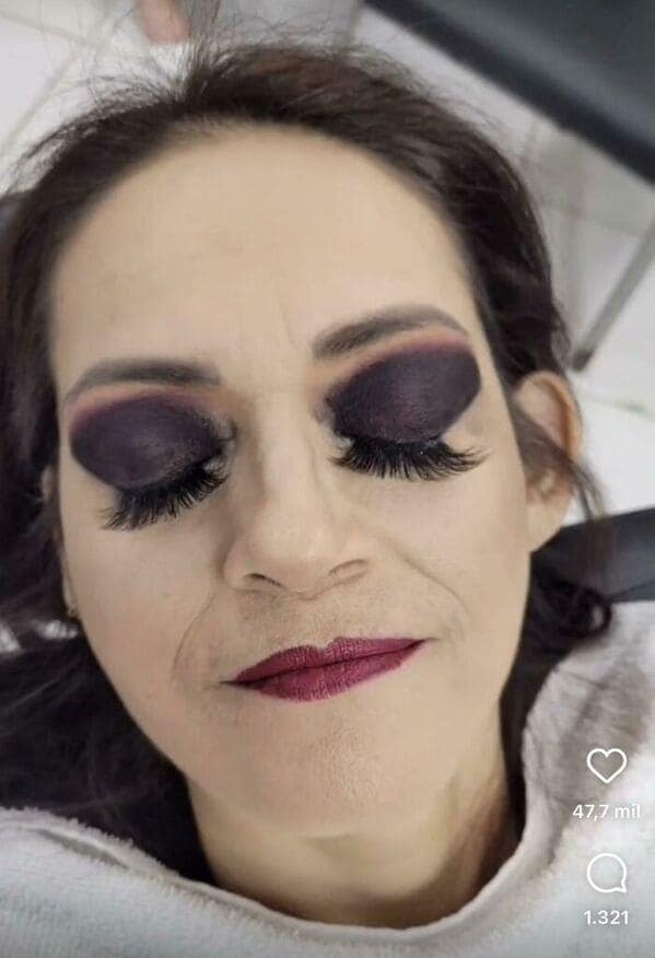 A severe makeup fail involving solid, unblended matte black eyeshadow that covers the entire eyelid like ink, paired with a dark berry lipstick and heavy, drooping false lashes.