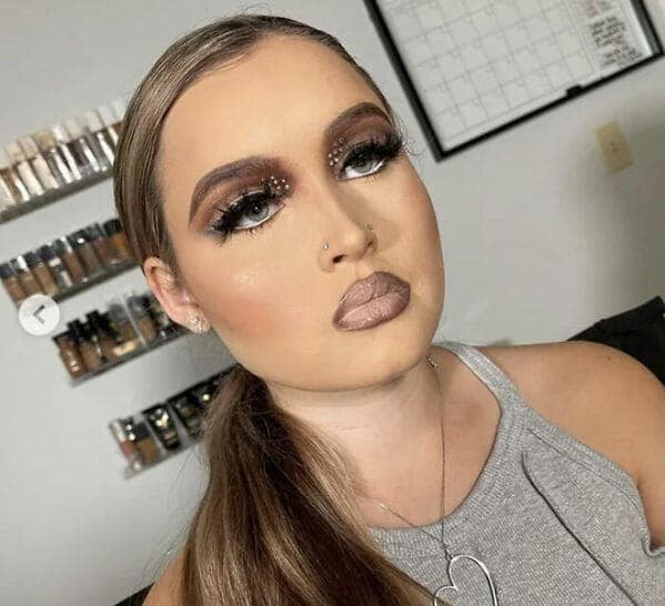 A makeup fail featuring "concealer lips" with a muddy greige lipstick that blends into the skin. The look is defined by extremely thick, dark blocky eyebrows and heavy, unblended brown nose contouring.