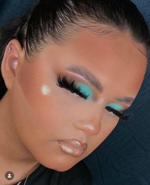 A side-profile makeup fail displaying a massive, unblended brown stripe of contour across the cheekbone and temple. The intense bronzer clashes with neon teal eyeshadow and extremely chunky, spidery false lashes.