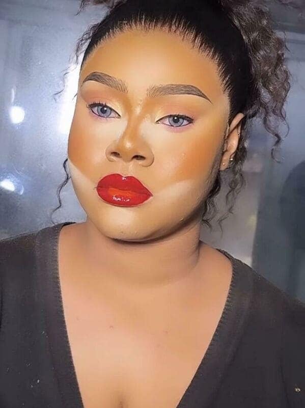 A classic makeup fail showcasing a severe "mask" effect. The subject has bright orange foundation that stops abruptly at the chin, leaving a startling white line along the jaw and neck, paired with a bold red lip and unblended, sharp nose contouring.