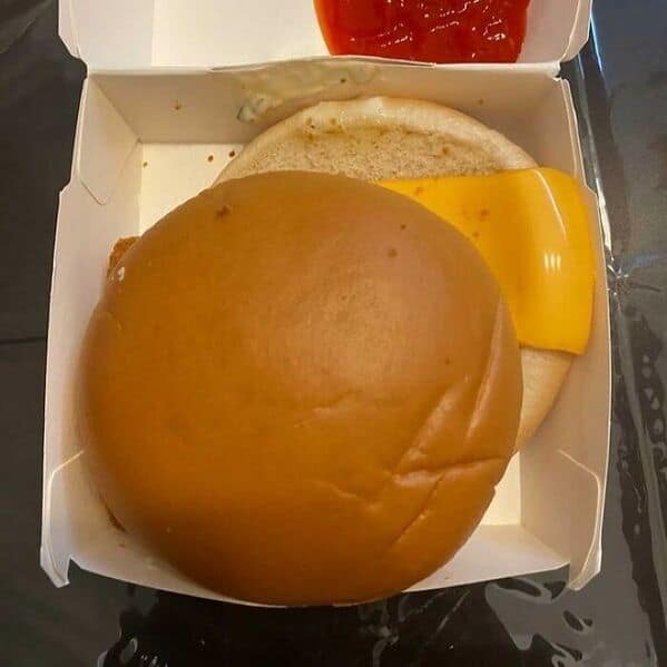 McDonald's burger assembly fail with patty misaligned on bun showing cheese hanging over edge