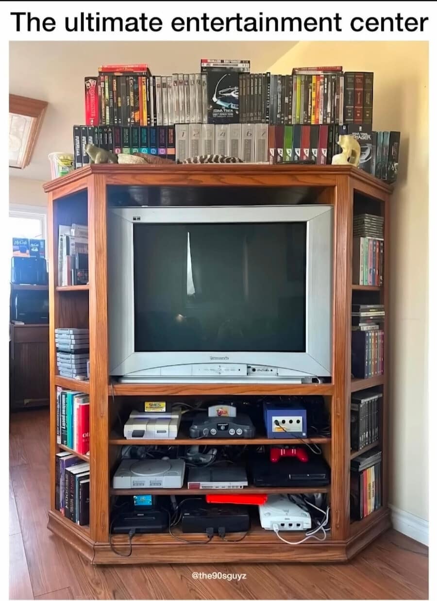 A nostalgic photo titled "The ultimate entertainment center" featuring a massive 90s-era wooden cabinet. It is perfectly optimized with a silver CRT television and a shelf for every classic console including a Sega Genesis, SNES, N64, GameCube, PS1, and Dreamcast.