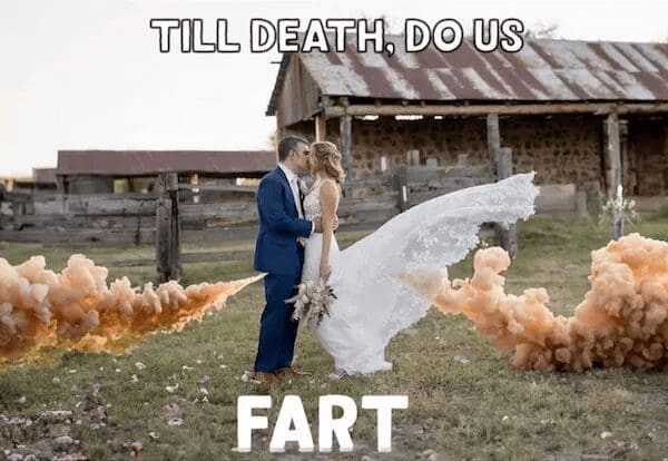 A satirical wedding photo showing a bride and groom kissing in front of a rustic barn. Two large plumes of orange smoke from smoke bombs are positioned perfectly behind the groom, making it look like an explosive gastrointestinal event. Bold white text reads: "TILL DEATH, DO US FART."
