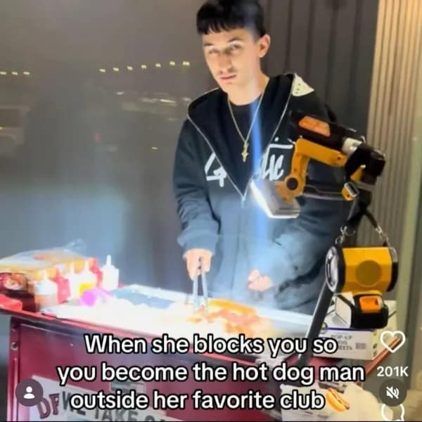 A grainy video-style capture of a young man with a bowl cut working a street hot dog cart at night. The text overlay suggests a bizarrely dedicated revenge plot: "When she blocks you so you become the hot dog man outside her favorite club."