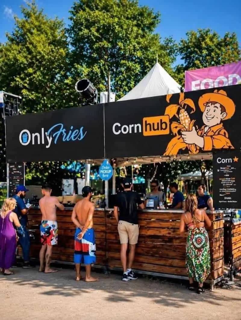 A funny meme showing a wide shot of a summer food festival. Two adjacent stands have banners parodying famous adult websites: "OnlyFries" using the OnlyFans logo style and "Corn hub" using the Pornhub logo style.