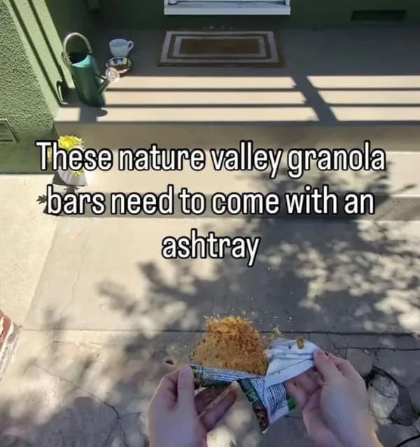 A POV shot of a tragic snack moment: a Nature Valley granola bar that has completely disintegrated into a pile of sawdust-like crumbs inside its wrapper. The text overlay suggests these bars are so messy they "need to come with an ashtray" to catch the debris.