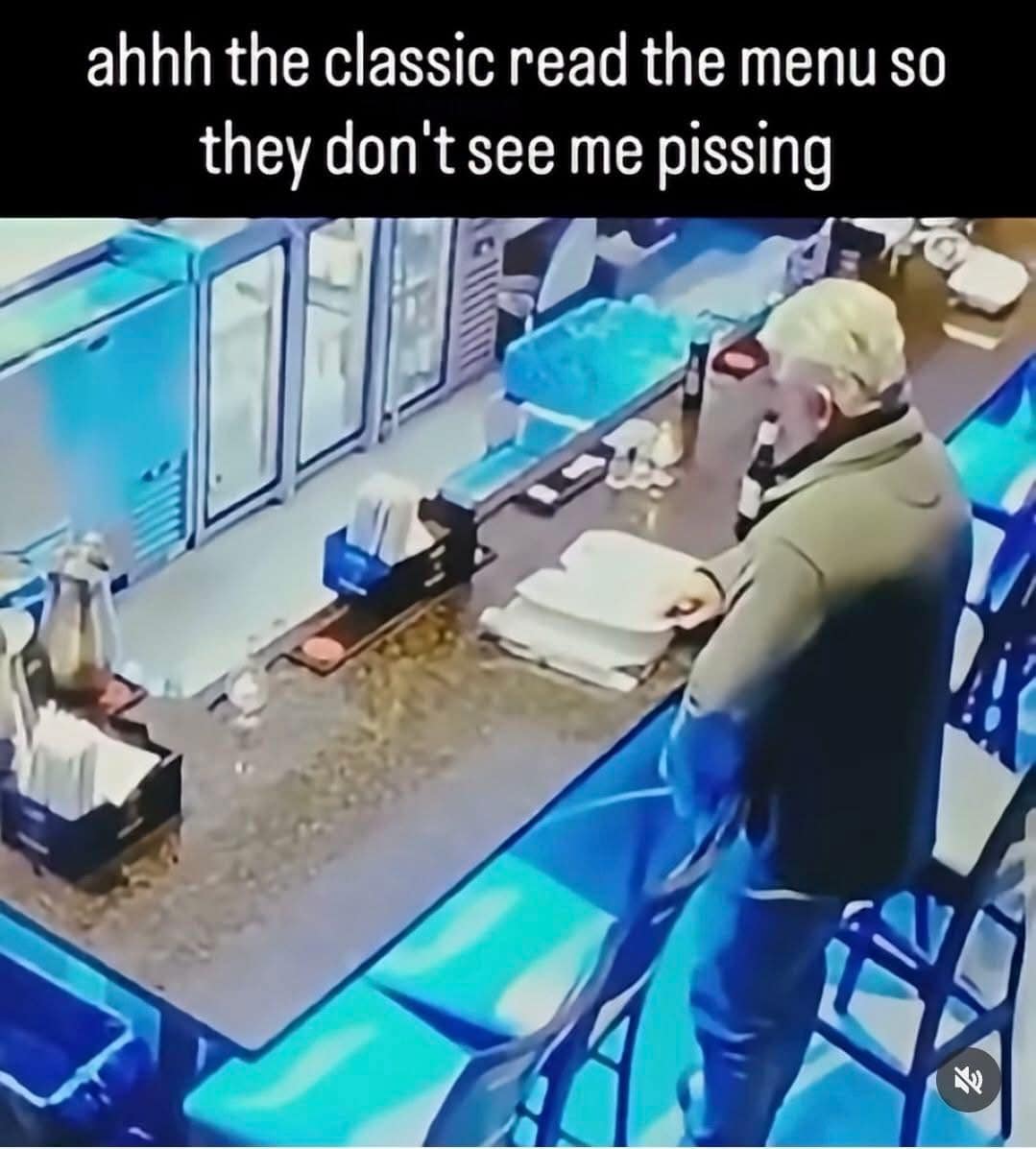A grainy, blue-tinted CCTV still used as a funny meme. It shows an older man standing at a bar, holding a beer and staring with unnatural intensity at a large open menu. The caption reads: "ahhh the classic read the menu so they don't see me pi*sing."