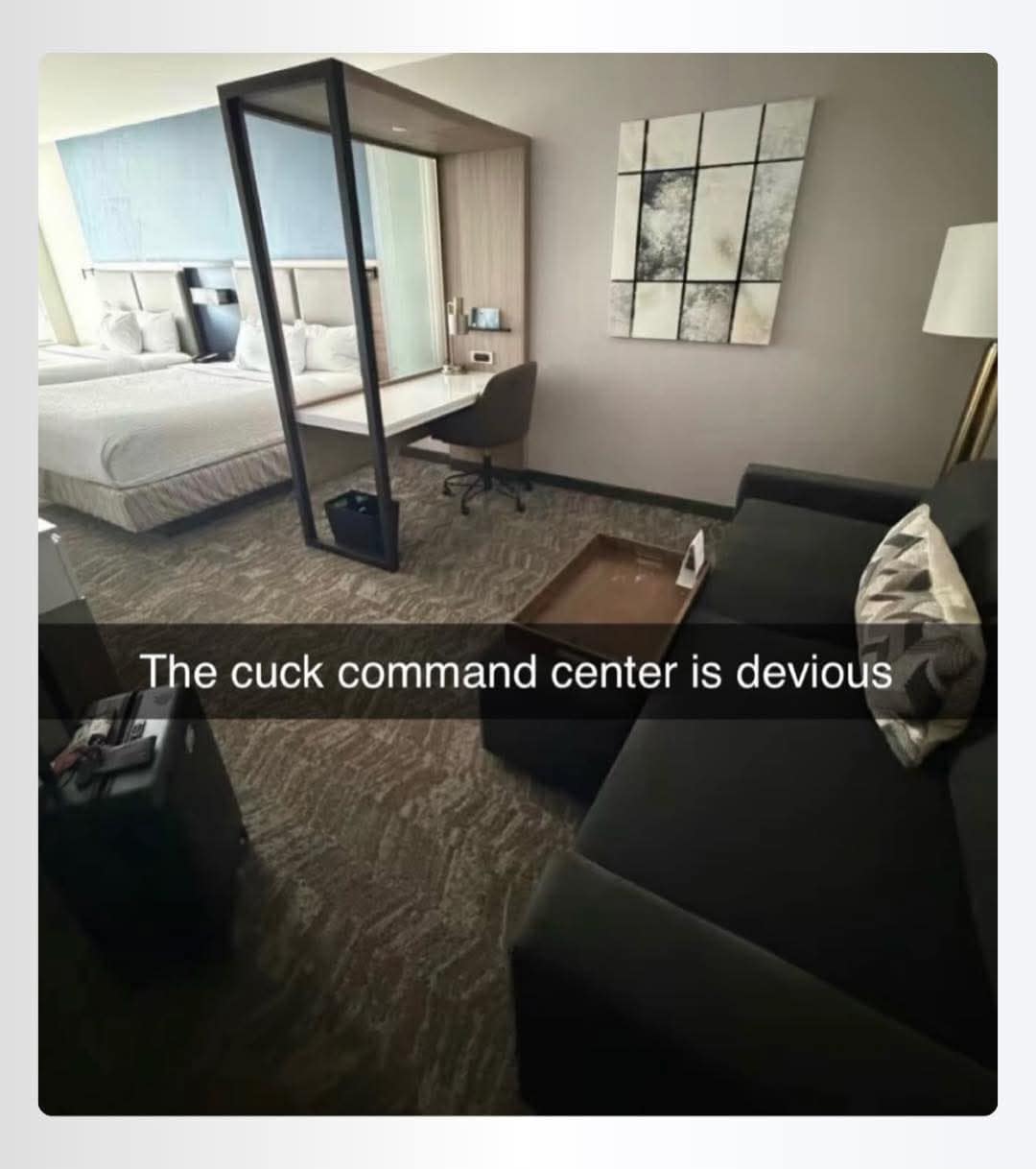 A meme dump photo of a confusingly designed hotel room where a workspace desk is enclosed in a glass and wood frame directly facing the two beds. A Snapchat-style caption floating in the center of the image reads: "The cuck command center is devious."