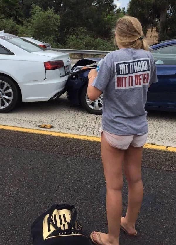 A perfectly timed ironic photo for any meme dump. A woman stands on the side of a highway next to a car accident she was involved in. Her t-shirt, visible from the back, features the unfortunate slogan: "HIT IT HARD, HIT IT OFTEN."