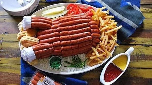 A culinary "cursed image" showing a massive platter arranged to look like a Thanksgiving turkey, but the "bird" is constructed entirely out of dozens of hot dogs bundled together. It is served with a side of french fries, pickles, and a split gravy boat of ketchup and mustard.