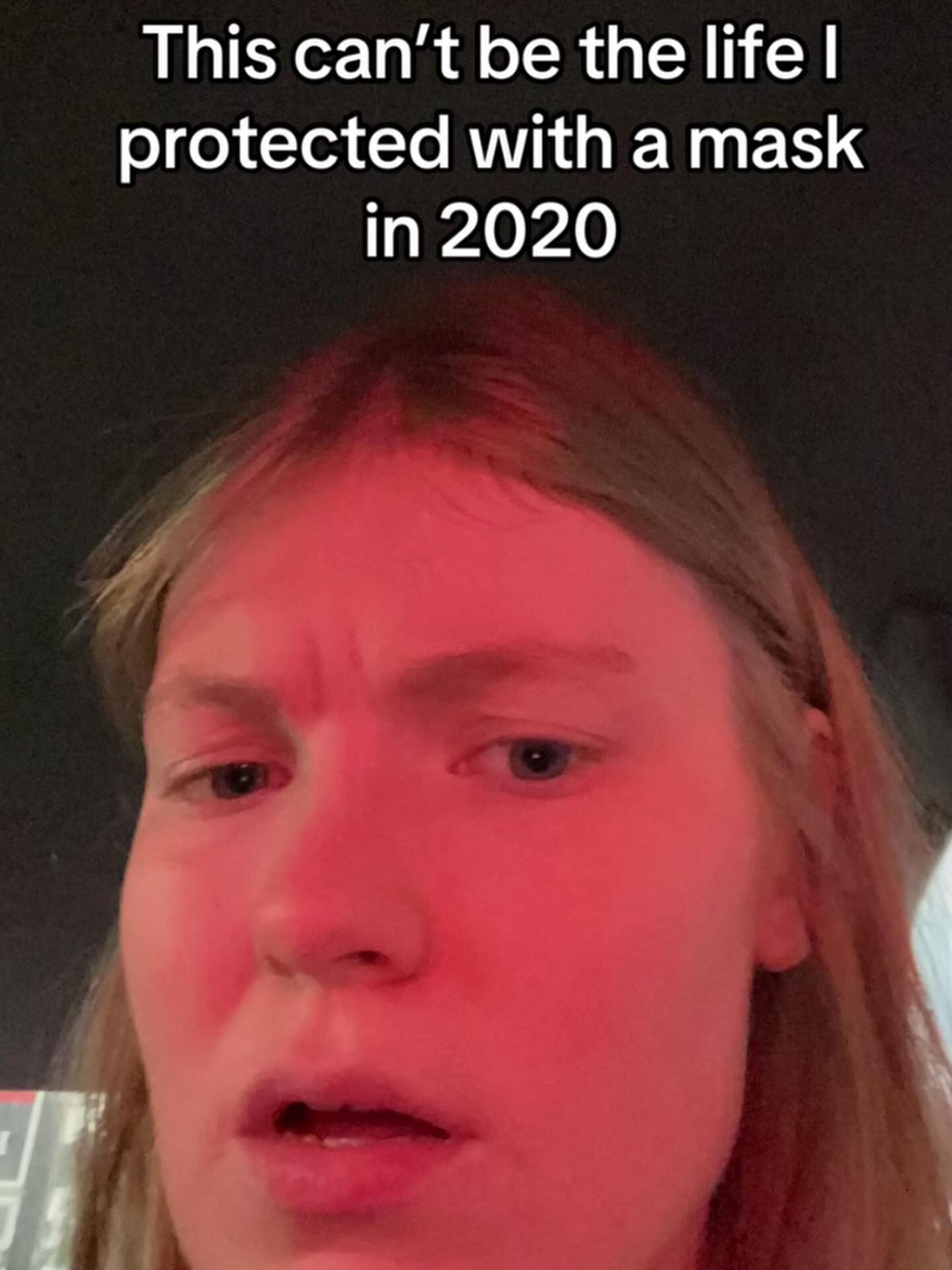 A close-up selfie of someone looking deeply skeptical and weary under a harsh red light. The text overlay reads, "This can't be the life I protected with a mask in 2020," capturing the collective existential dread of the post-pandemic world in a funny meme.