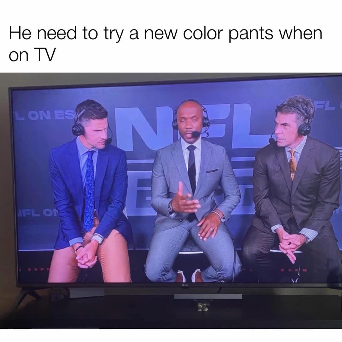 A screenshot of a live NFL broadcast that has become a funny meme. Three male commentators sit on stools, but the man on the far left is wearing tan pants that match his skin tone so perfectly he appears to be sitting there without any pants on at all.