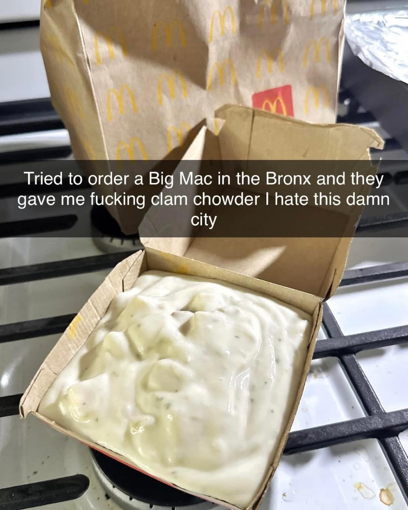 A disastrous food-fail meme dump photo showing a McDonald's Big Mac box filled to the brim with thick, chunky clam chowder instead of a burger. The caption laments, "I hate this damn city."