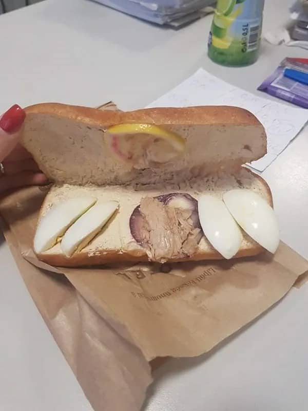 Open sub sandwich with uneven toppings — tuna, hard-boiled egg slices, and lemon wedge