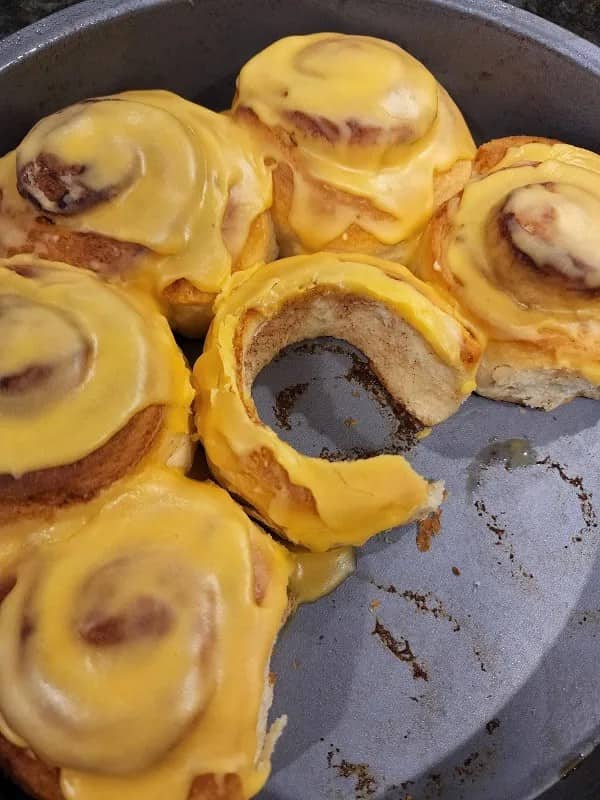 Cinnamon rolls topped with yellow frosting resembling melted cheese, one roll missing its center
