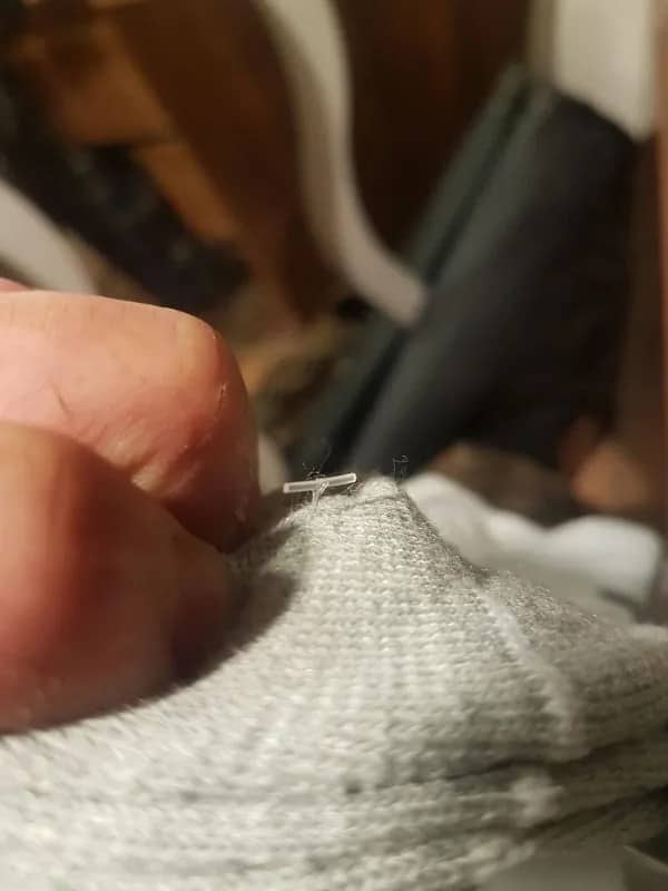 Plastic retail tag fastener stubbornly embedded deep in grey knit sweater fabric