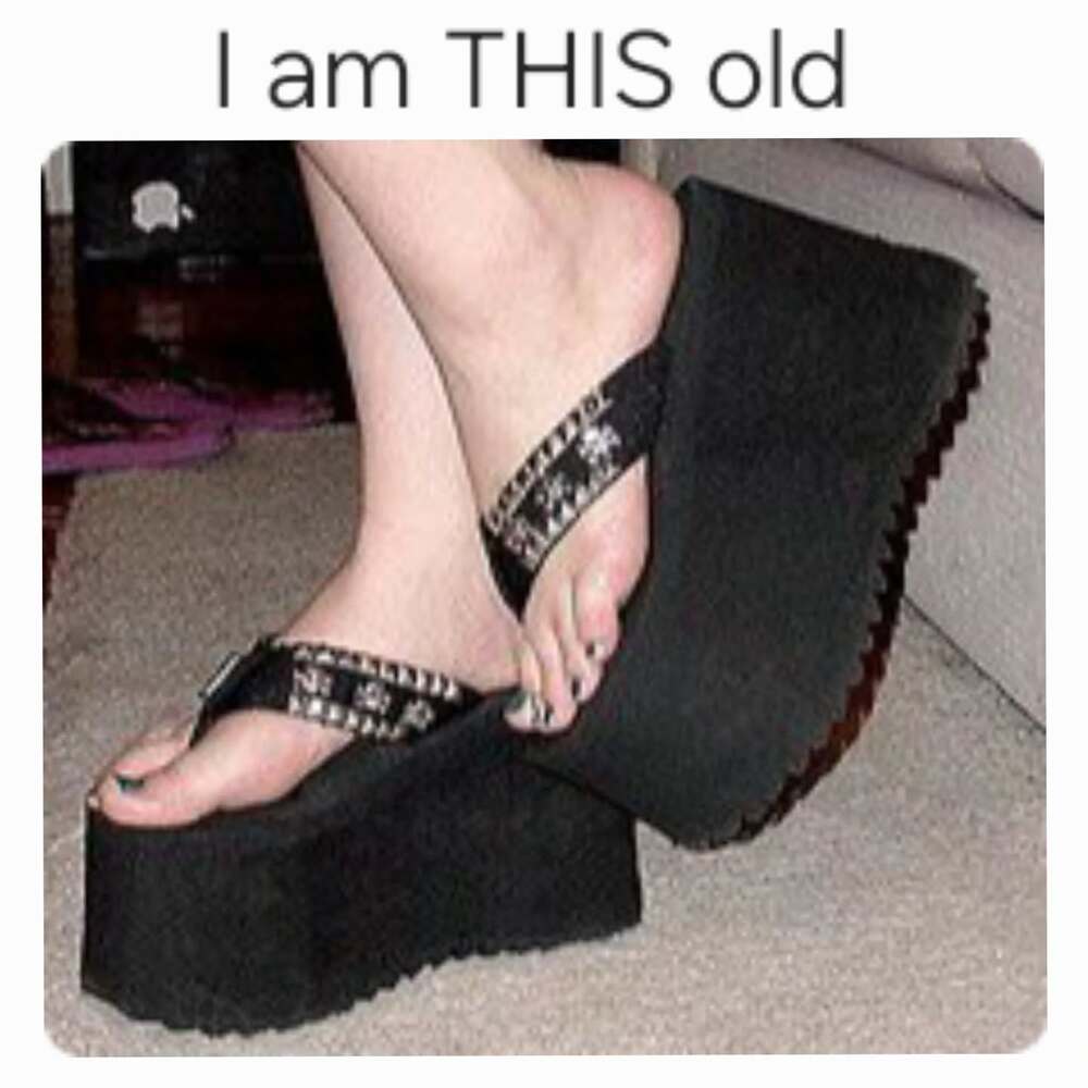 A pair of black foam platform flip-flops with "Steve Madden" energy are shown in this millennial meme. The extreme height of the wedge sole and the tropical patterns on the straps serve as a definitive "I am THIS old" marker.