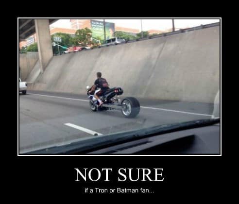 A bizarre visual motorcycle meme of a custom sportbike on a highway featuring an impossibly long extended swingarm and a massive, wide car tire on the back. The text asks the question we're all thinking: "NOT SURE if a Tron or Batman fan..."
