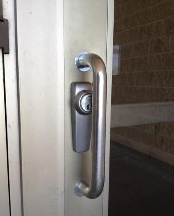 A design nightmare and cursed image showing a commercial door handle that has been installed directly on top of the lock cylinder, making it physically impossible for anyone to ever insert a key into the door.