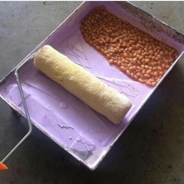 classic cursed image featuring a plastic paint tray where the reservoir is inexplicably filled with a thick, saucy layer of baked beans instead of paint, with the roller resting ready to spread the legumes across a wall.