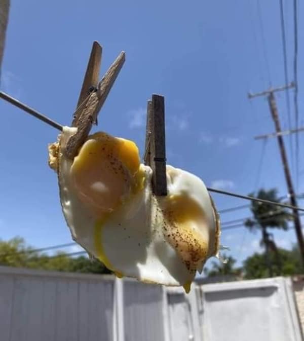 surreal cursed image of two sunny-side-up fried eggs hanging from an outdoor wire clothesline, secured by old-fashioned wooden clothespins against a clear blue sky.