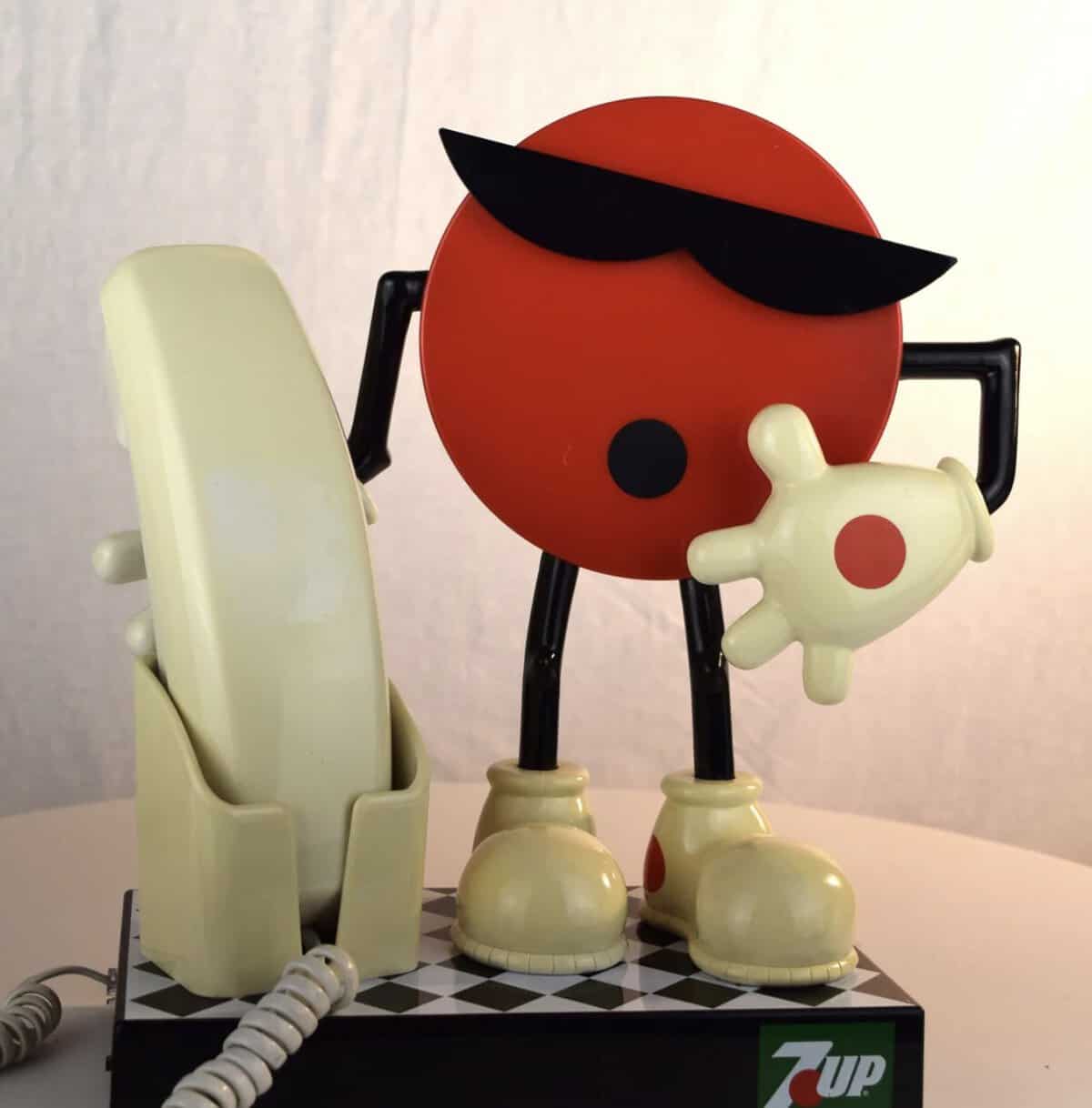 1990s novelty landline phone featuring the 7-Up mascot, "Cool Spot." The red circular character wears sunglasses and white sneakers, standing next to a cream-colored handset