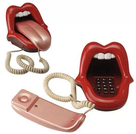 novelty landline phone depicting a pair of glossy red lips with white teeth. The handset is a matching pink tongue that rests inside the open mouth, while the base contains a concealed black numerical keypad.