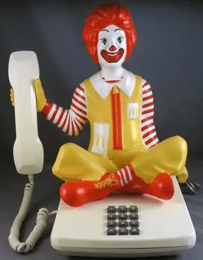rare vintage landline phone featuring a large, seated Ronald McDonald figure. The iconic clown mascot holds a standard beige handset to his ear, with the keypad built directly into the white square base he is sitting on.