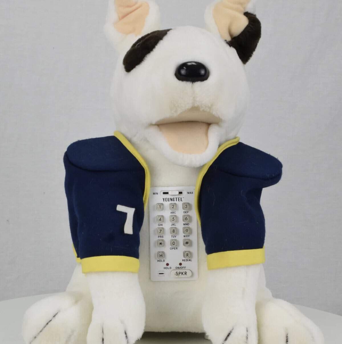 A soft-sculpt novelty landline phone designed like a plush bull terrier wearing a blue football jersey. A white numerical keypad is integrated into the dog's chest, turning the stuffed animal into a functional communication device.