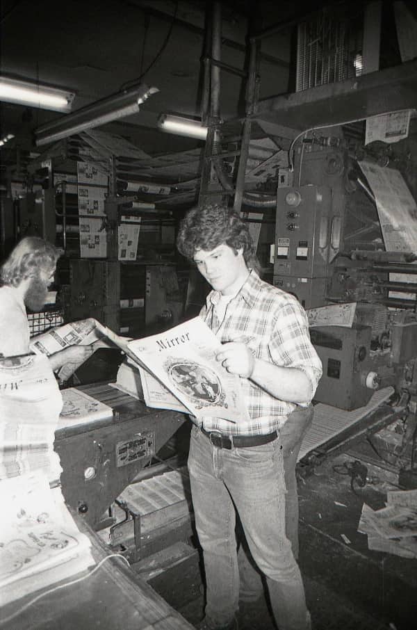 Young man in plaid shirt reading fresh newspaper print in vintage industrial press room