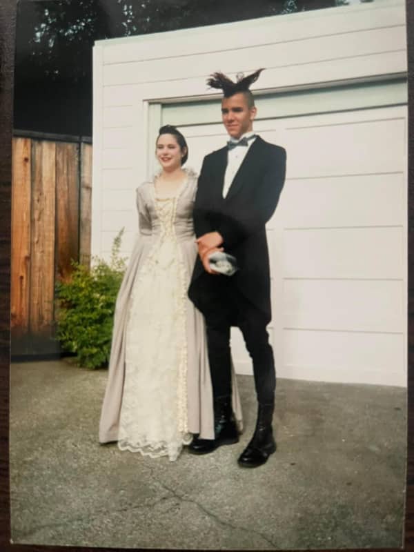 90s prom couple posing outside — girl in lace gown, boy sporting dramatic spiked mohawk tuxedo