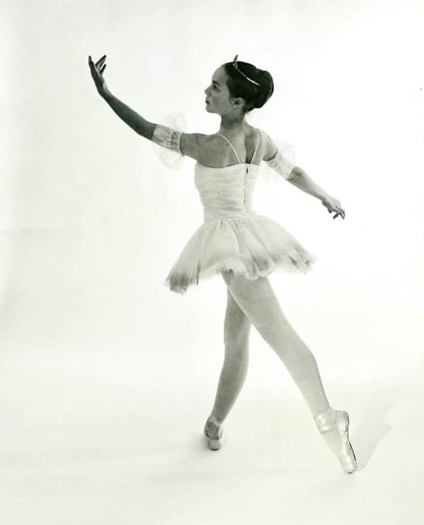 Young ballerina in white tutu and pointe shoes performing graceful pose in black and white studio photo