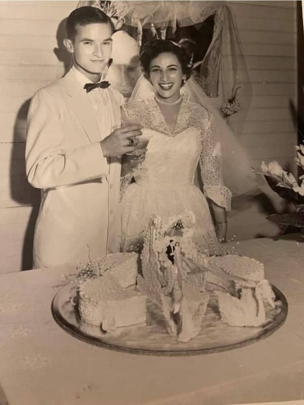 1950s bride and groom smiling beside already-sliced wedding cake at vintage reception celebration