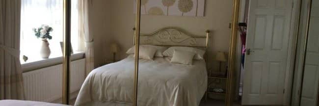Mirrored wardrobe doors in bedroom reflecting cozy floral bedding and window with flowers