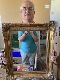 Ornate gold framed mirror for sale held up by older man with glasses smiling