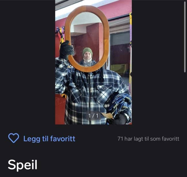 Oval wooden framed mirror for sale held in front of face reflecting bundled up man