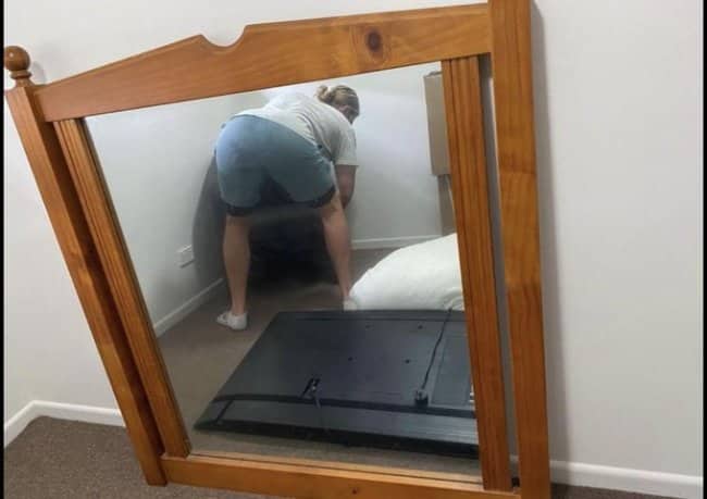 Wooden framed mirror for sale reflecting woman bending over assembling TV stand on floor