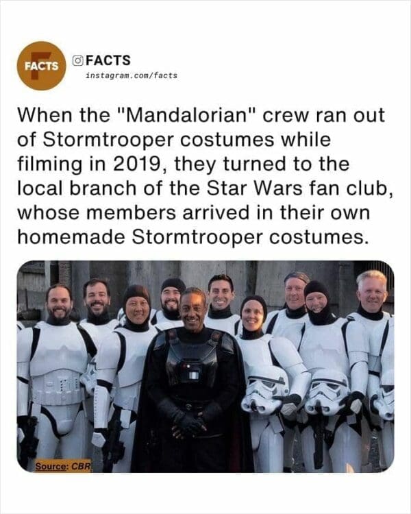 behind-the-scenes random facts photo from the set of The Mandalorian. It shows actor Giancarlo Esposito posing with a group of fans in Stormtrooper armor. The text reveals that in 2019, the crew ran out of costumes and had to recruit local Star Wars fan club members who had their own high-quality, homemade gear.