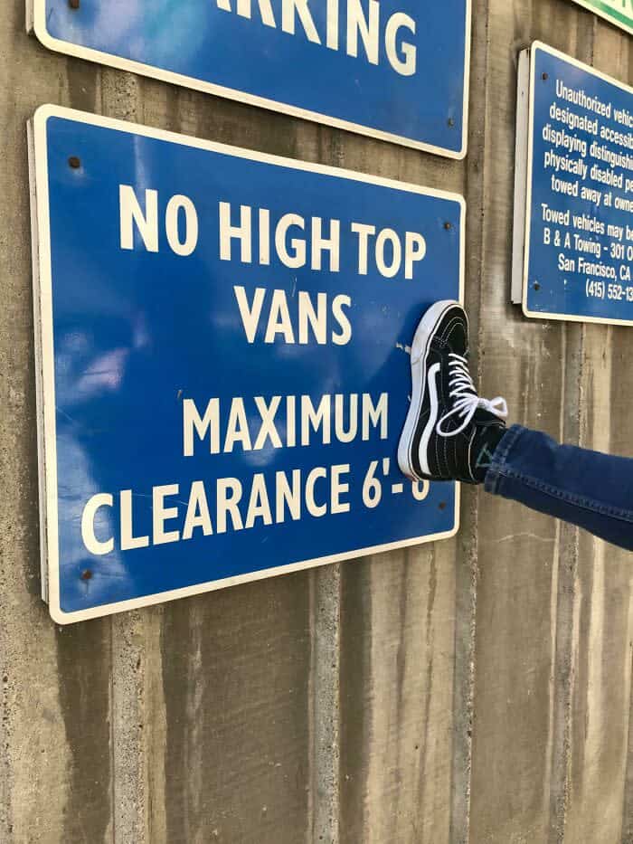 Person wearing Vans sneaker kicks sign reading No High Top Vans maximum clearance six feet