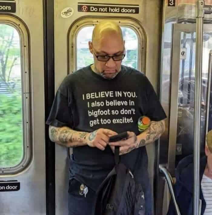 Tattooed man on subway wearing shirt saying I believe in Bigfoot so don't get excited