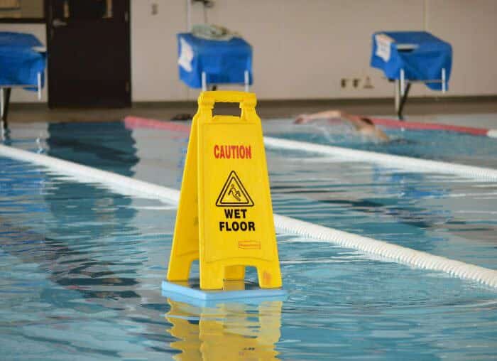 Yellow caution wet floor sign floating inside an indoor swimming pool lane