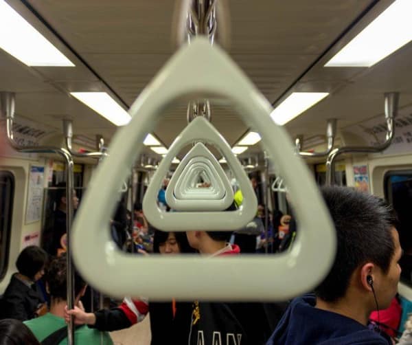 A perspective-bending satisfying photo taken from inside a subway car, where the triangular overhead hand straps align in a perfect, repeating vanishing point that tunnels through the center of the frame.