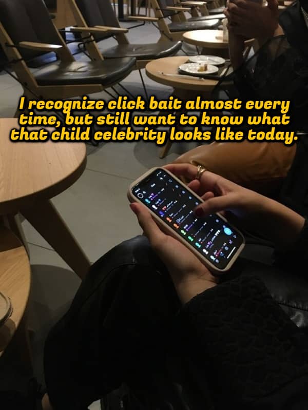 Person holding a smartphone in a cafe displaying a shower thought about clickbait articles.