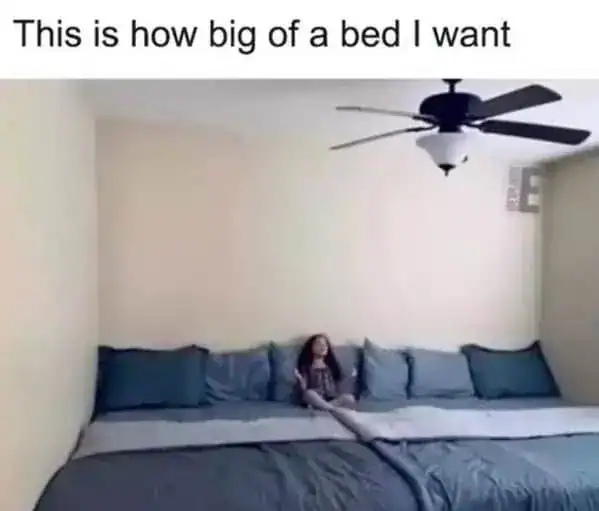 aspirational sleep meme showing a child sitting in the middle of a massive, wall-to-wall bed that fills the entire room under a ceiling fan. The text declares, "This is how big of a bed I want," representing the ultimate sleep sanctuary.