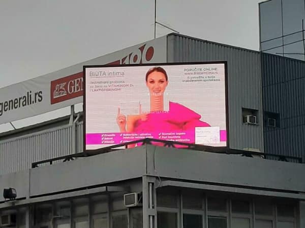 A massive rooftop digital billboard experiencing a hilarious alignment tech fail, where a shifted screen panel has transformed a standard medical ad into a woman with a three-foot-long "giraffe" neck.