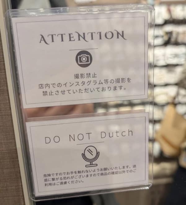 confusing translation fail on a retail notice. The top sign correctly forbids photography and Instagramming, but the bottom sign, intended to stop people from touching or using display mirrors, simply reads: "DO NOT Dutch."
