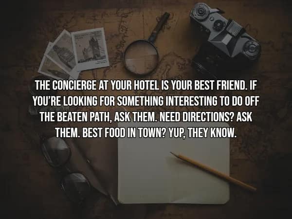 A travel hack tip suggesting that the hotel concierge is a traveler's best friend for finding hidden gems and local food. The white text is overlaid on a tabletop scene with a world map, a vintage film camera, and a pair of reading glasses.