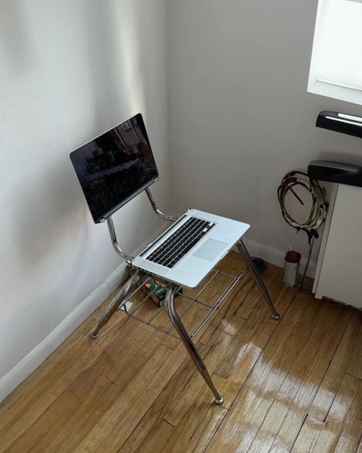 MacBook laptop repurposed as chair backrest and seat creating improvised minimalist desk setup