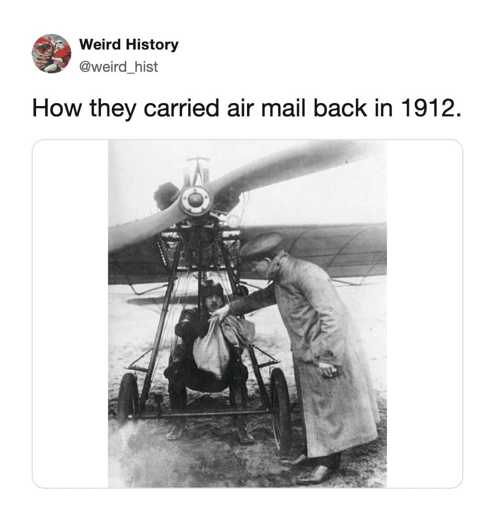 1912 black and white photograph of early pilot sitting in exposed open air biplane frame receiving a mail sack for air mail delivery