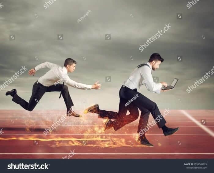 Strange weird stock photo of two businessmen racing on fiery track while one uses laptop